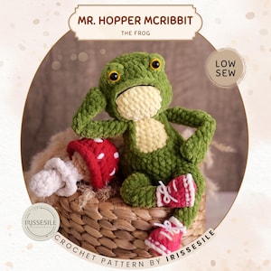 May include: A handmade green crochet frog named Mr. Hopper McRibbit, wearing red and white sneakers. The frog has yellow eyes and a cream-colored belly. A red and white mushroom is next to the frog. The text "CROCHET PATTERN BY IRISSESILE" is at the bottom.