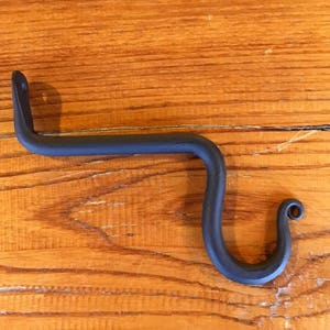 May include: Black metal hook with a curved design. The hook is made of wrought iron and has a rustic finish.