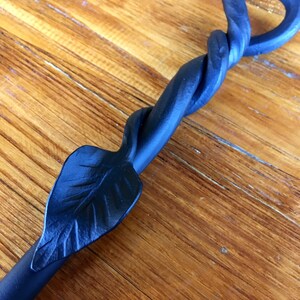 May include: Black metal fireplace poker with a twisted handle and a leaf design at the end.