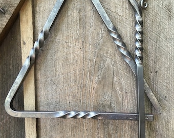 Puede incluir: Un triángulo de metal retorcido con un percutor de metal retorcido. El triángulo está colgado de un clavo en una superficie de madera.