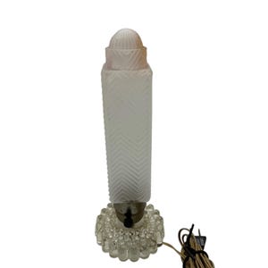 May include: A vintage table lamp with a clear, textured base and a frosted glass shade. The shade has a chevron pattern and a rounded top. The lamp has a cord and plug.