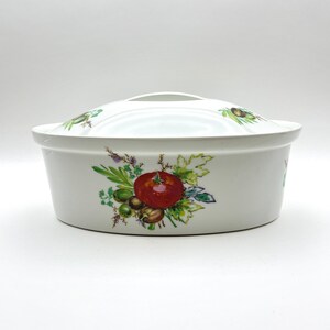 May include: White ceramic oval baking dish with a lid. The dish has a floral design featuring a red tomato, green leaves, and brown olives.