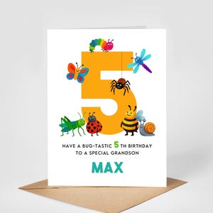May include: A birthday card featuring a large orange number 5, adorned with cartoon insects. The card's message is "Have a bug-tastic 5th birthday to a special grandson" with the name "MAX" below. The card rests on a brown envelope.