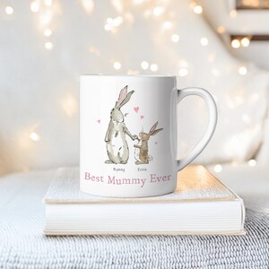 Pu&ograve; includere: Una tazza in ceramica bianca con un'illustrazione disegnata a mano di due conigli che si tengono per mano. Il testo "Best Mummy Ever" &egrave; stampato sulla tazza. I conigli sono etichettati come "Mummy" e "Rosie".