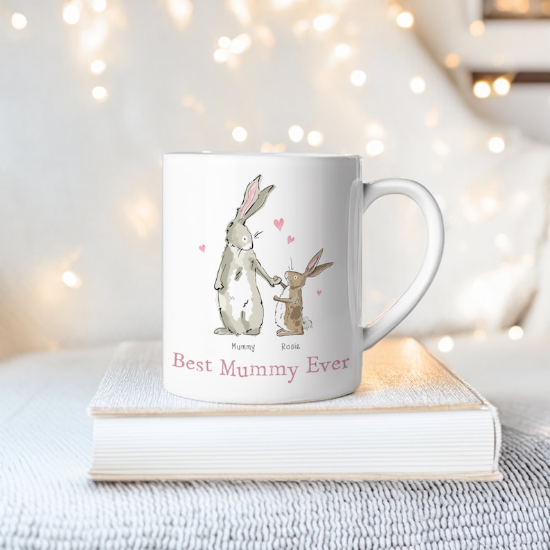Pu&ograve; includere: Una tazza in ceramica bianca con un'illustrazione disegnata a mano di due conigli che si tengono per mano. Il testo "Best Mummy Ever" &egrave; stampato sulla tazza. I conigli sono etichettati come "Mummy" e "Rosie".