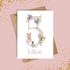 May include: A white card with a pink polka dot background featuring a large number 5 with four fairies surrounding it. The fairies are wearing pink, purple, and blue dresses with wings. The name Lillian is written below the number.