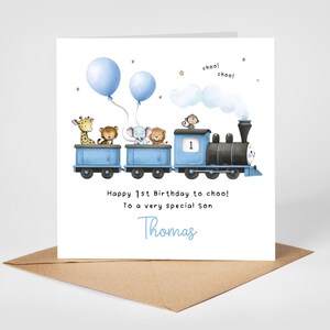 May include: A birthday card featuring a blue train with animal passengers, including a giraffe, tiger, elephant, lion, and monkey. Two blue balloons float above the train. The card reads "Happy 1st Birthday to choo! To a very special son Thomas."