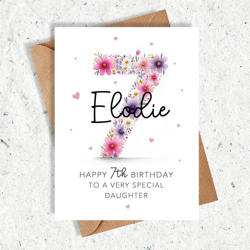May include: A white birthday card with a floral number seven, pink hearts, and the name "Elodie" in black script. The card reads "Happy 7th Birthday to a very special daughter."
