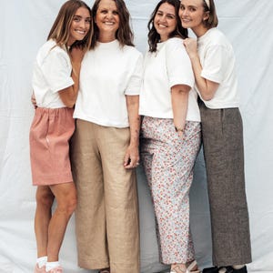 May include: Four women wearing white t-shirts and different pants. The woman on the left is wearing pink shorts, the woman in the middle is wearing beige pants, the woman on the right is wearing floral pants, and the woman on the far right is wearing gray pants.