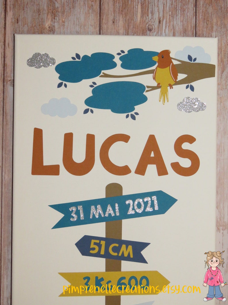 K&ouml;nnte beinhalten: Eine beige Leinwand mit einem braunen Ast mit blauen und wei&szlig;en Wolken. Ein gelber Vogel sitzt auf dem Ast. Ein braunes Schild mit dem Text "LUCAS" befindet sich &uuml;ber einem braunen Pfosten mit drei Schildern. Das oberste Schild ist blau mit dem Text "31 MAI 2021". Das mittlere Schild ist blau mit dem Text "51 CM". Das unterste Schild ist gelb mit dem Text "3 KG 600".