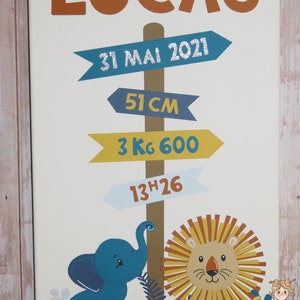 K&ouml;nnte beinhalten: Ein wei&szlig;es Leinwand-Schild mit dem Namen "Lucas" in orangefarbenen Buchstaben. Das Schild hat blaue, gelbe und hellblaue Pfeile mit dem Text "31 Mai 2021", "51 cm", "3 kg 600" und "13h26". Das Schild zeigt auch einen blauen Elefanten und einen gelben L&ouml;wen.