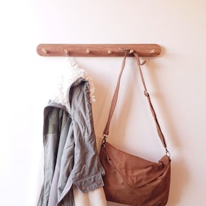 May include: A wooden coat rack with five hooks, a green jacket with a white fleece lining, and a brown leather shoulder bag hanging from the hooks.