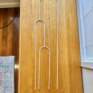 May include: Three white metal plant supports, each with a rounded top, arranged in a vertical stack on a wooden surface.