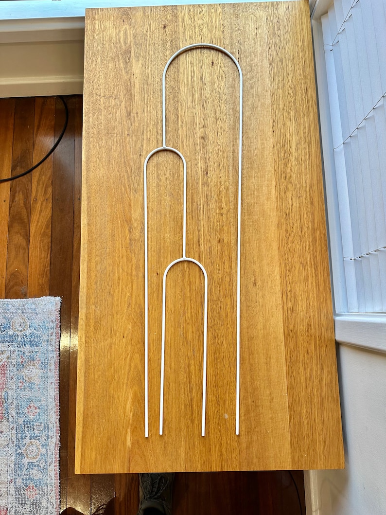 May include: Three white metal plant supports, each with a rounded top, arranged in a vertical stack on a wooden surface.