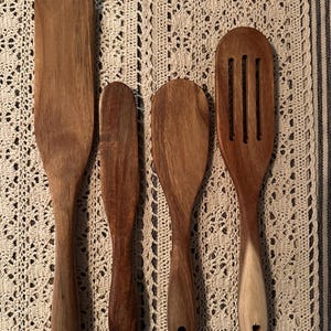 May include: Four wooden kitchen utensils, including a spatula, a spoon, and two spatulas with different shapes. The utensils are all made of dark brown wood and have a natural finish.