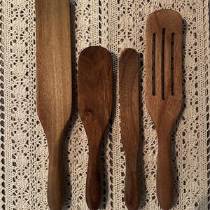 May include: Four wooden kitchen utensils, including a spatula, a spoon, a knife, and a flat paddle, all with brown wood handles.