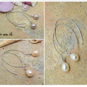 May include: A pair of silver dangle earrings with a teardrop-shaped pearl on each earring. The pearls are a light pink color. The earrings are on a light brown textured surface.