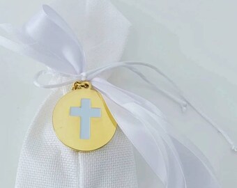 May include: A white fabric bag with a white satin ribbon tied around it. A gold round charm with a white cross is attached to the bag.