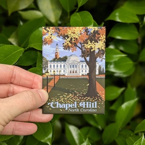May include: A vintage-style illustration of a building with a clock tower and the text "Chapel Hill, North Carolina". The building is surrounded by trees with fall foliage.