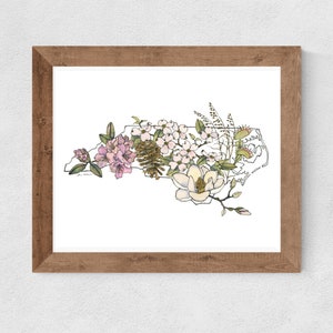 May include: A line drawing of the state of North Carolina with various flowers and plants growing out of the outline. The flowers are pink, white, and yellow. The plants are green. The state name is written at the bottom of the outline.