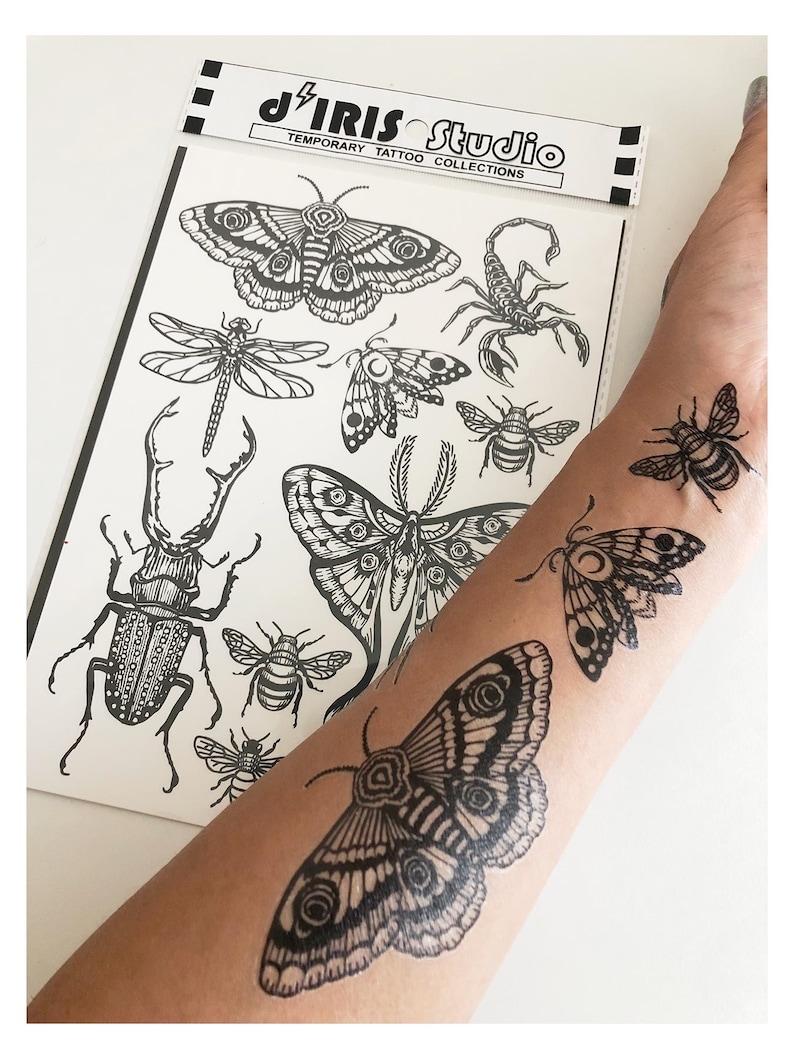 May include: A sheet of black and white temporary tattoos from J'IRIS STUDIO TEMPORARY TATTOO COLLECTIONS featuring detailed illustrations of insects including moths, a beetle, a dragonfly, a scorpion, and bees, with three applied to skin.