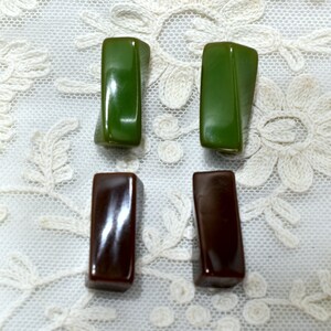 May include: Four rectangular shaped buttons, two are dark green and two are dark brown. The buttons are on a white lace background.