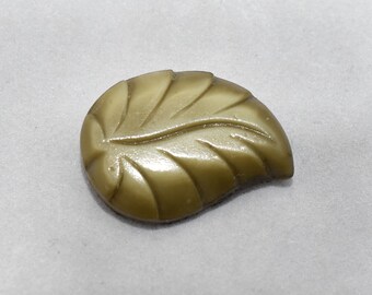May include: A green leaf-shaped button with a raised design. The button is made of plastic and has a glossy finish.