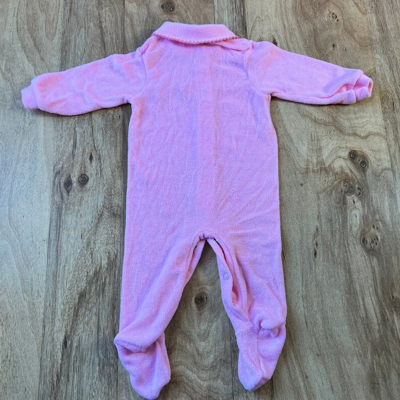 May include: A pink baby onesie with a collared neckline. The onesie is made of a soft, fuzzy material.