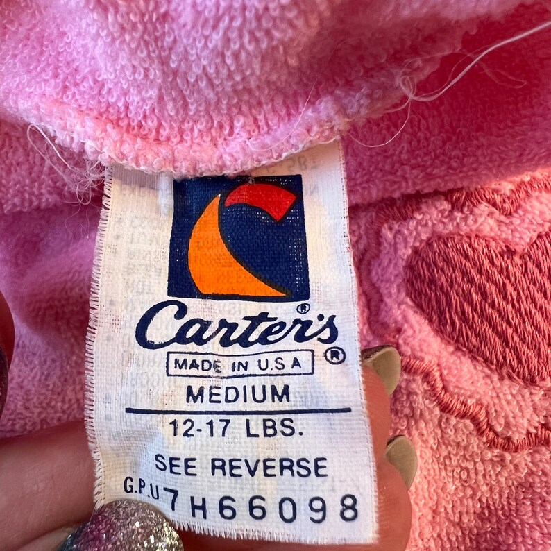 May include: White tag with blue and orange logo for Carter's. The tag says "Made in USA", "Medium", "12-17 LBS", "See Reverse", and "G.P.U. 7H6 6098".