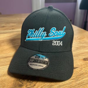 Può includere: Cappellino da baseball nero con un logo ricamato bianco e blu che dice "Philly Soul 2004". Il cappello ha un logo New Era nero e il testo "39THIRTY MEDIUM-LARGE" sul retro.