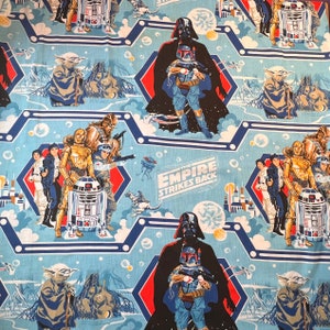 May include: Light blue fabric featuring Star Wars characters like Darth Vader, Boba Fett, Yoda, and R2-D2. The design includes the text "Star Wars: The Empire Strikes Back" and is set against a geometric pattern with red and white accents.