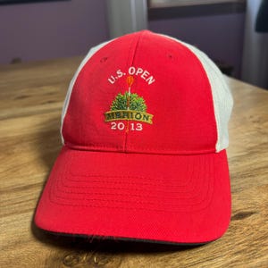 Op de afbeelding: Rode en witte baseballpet met een geborduurd logo met de tekst "U.S. Open Merion 2013".