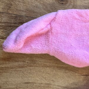 May include: Close-up of a pink fleece fabric with a soft texture. The fabric is folded over on itself, creating a smooth, rounded edge.