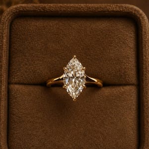 Op de afbeelding: Een gouden ring met een grote marquise-geslepen centrale steen die door zes klauwen wordt vastgehouden. De ringband is glad en gepolijst en heeft een taps toelopend ontwerp dat aansluit op de zetting. De steen is helder en gefacetteerd.
