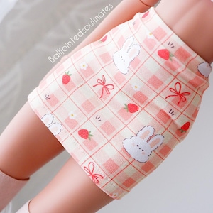 May include: A pink and white checkered skirt with a bunny and strawberry print. The skirt is made of a soft, stretchy fabric and has a comfortable fit.