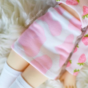 Peut inclure: Une jupe rose et blanche &agrave; motif vache. La jupe est faite d'un tissu doux et extensible et a une coupe confortable. La jupe est associ&eacute;e &agrave; des chaussettes blanches montantes.