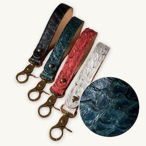 Pode incluir: Quatro porta-chaves de pulso com padrões texturizados semelhantes a escamas em preto, verde escuro, vermelho e prateado. Cada alça é fixada com um rebite de metal cor de latão e inclui um mosquetão giratório a condizer em latão.