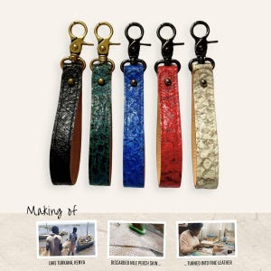 Könnte beinhalten: Fünf Schlüsselanhänger aus Leder mit strukturierter Oberfläche in Schwarz, Grün, Blau, Rot und Cremeweiß. Jeder hat einen Metallkarabiner und eine Niete. Der Text lautet: Making of, Lake Turkana, Kenya, Discarded Nile Perch Skin, Turned into Fine Leather.