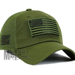 May include: Olive green baseball cap with a mesh back and a curved brim. Features a black embroidered American flag patch on the front and a smaller one on the side. The cap has a structured crown and a button on top.
