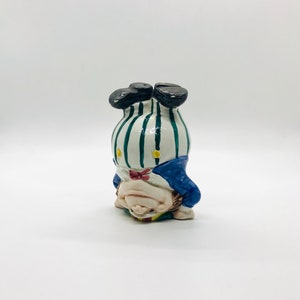 Könnte beinhalten: Eine Keramikfigur eines Menschen, der auf den Händen steht und ein blau-weiß gestreiftes Hemd, eine blaue Hose und eine rote Fliege trägt.