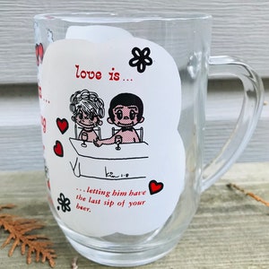 May include: A clear glass mug with a white design featuring a cartoon couple and the text "love is... letting him have the last sip of your beer."