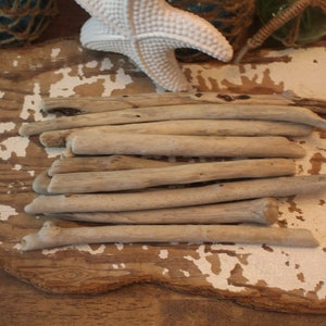 May include: A collection of driftwood sticks arranged in a stack on a weathered wooden surface. The sticks are various shades of gray and brown, with a natural, rustic look.