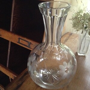 May include: A clear glass vase with a wide base and a narrow neck. The vase is decorated with etched floral designs.