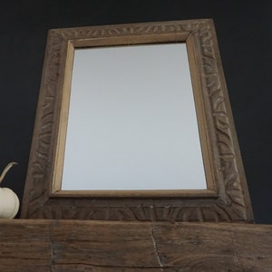 May include: A white pumpkin sits on a wooden mantel below a rectangular mirror with a carved wooden frame.