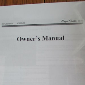 Könnte beinhalten: Eine schwarz-weiße Bedienungsanleitung für eine Husqvarna Viking Mega Quilter 18x8 Nähmaschine.
