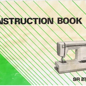 May include: A white sewing machine with a green and white striped instruction book. The book has the title "INSTRUCTION BOOK" and the model number "SR 2100".