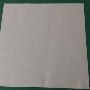 May include: A plain white square piece of paper on a green surface.