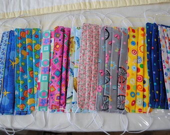 May include: A collection of 10 colorful fabric face masks with various patterns, including fruit, geometric shapes, flowers, and bicycles. The masks are all pleated and have white elastic ear loops.