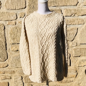 Peut inclure: Un pull en tricot torsadé de couleur crème avec un col rond et des manches longues. Le pull est fait d'un matériau doux et chaud et présente un motif en tricot torsadé irlandais traditionnel.