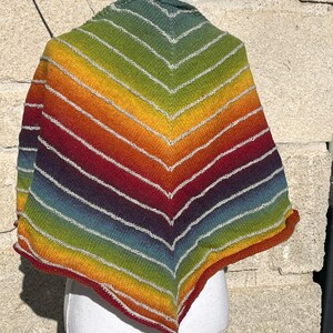 Peut inclure: Un châle fait main aux couleurs de l'arc-en-ciel, présenté sur un mannequin. Il présente des rayures rouges, oranges, jaunes, vertes et bleues. Le châle en tricot a une encolure en V et est fabriqué en fil.